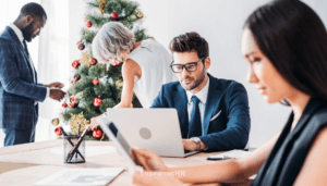 Two diverse coworkers share a desk, focusing on a computer screen and phone screen. Their collaboration embodies workplace inclusivity and diversity. The scene is representative of an inclusive holiday workplace.